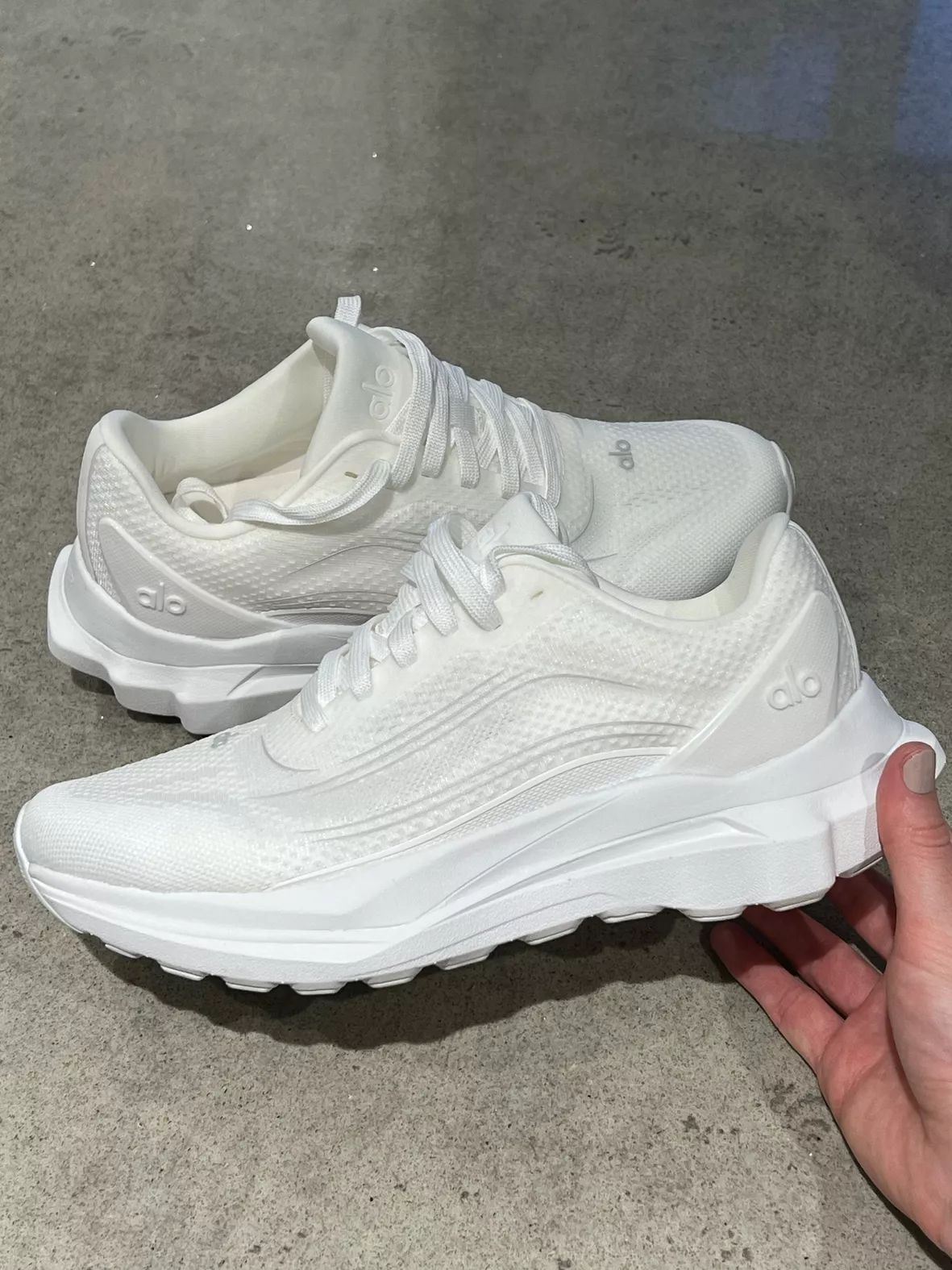 Pair of white ALO Runner sneakers shown by hand
