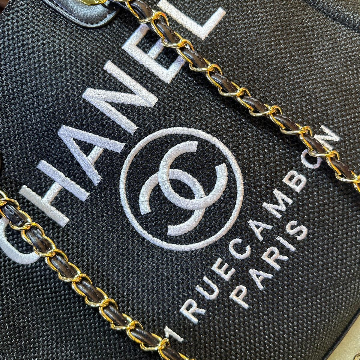 Close-up of a Chanel handbag with gold chain detail on a black background.