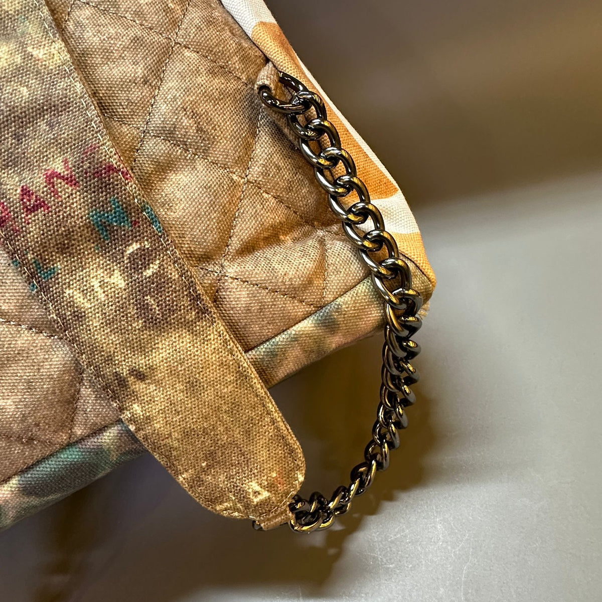 Close-up of a textured fabric pouch with a chain detail on a neutral background