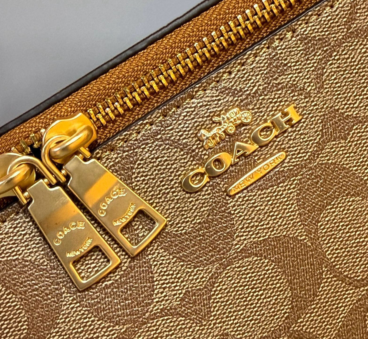 Close up of gold tone zipper pull and stamped Coach logo on signature canvas