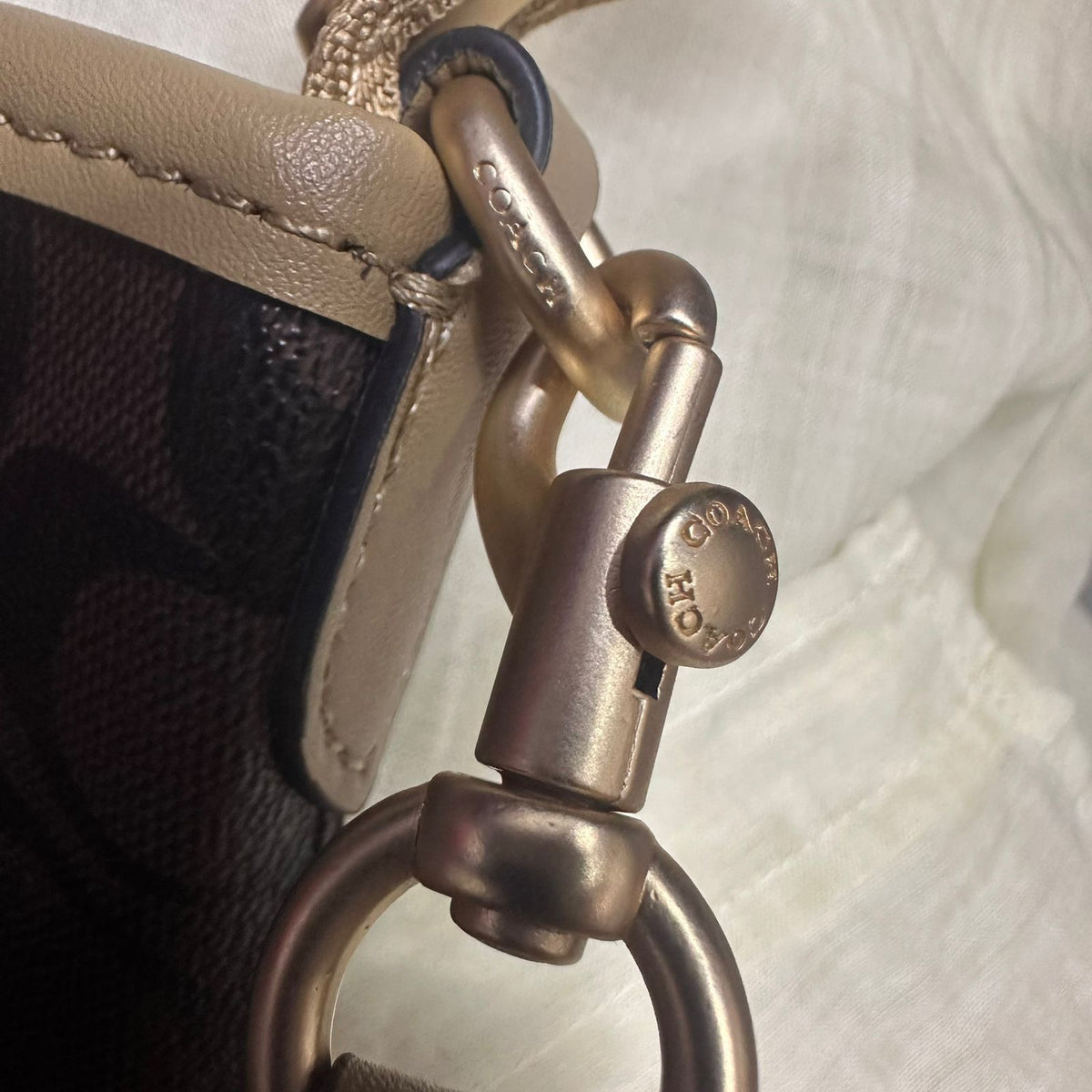 Close up of gold tone strap hardware clip on Coach signature bag
