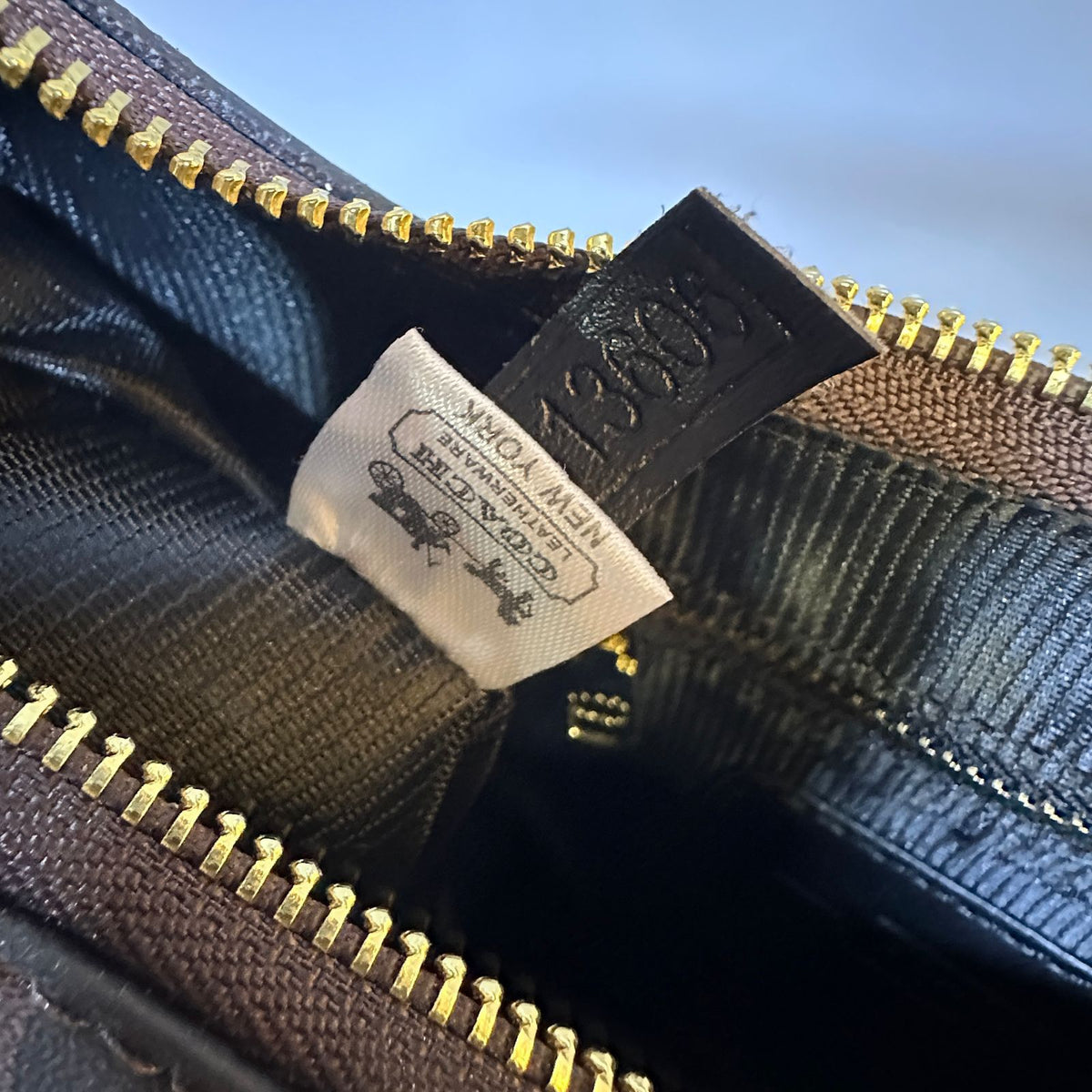Close-up of a label on a black leather product with gold zipper details.