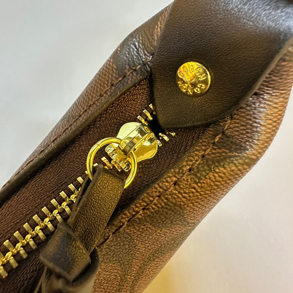 Brown leather pouch with gold zipper and logo on a light background