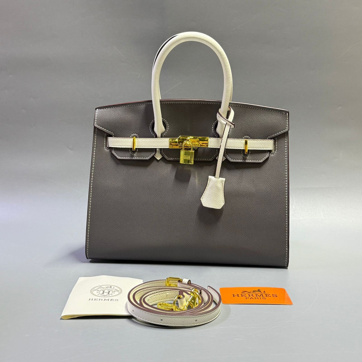 Dark grey luxury leather tote bag with white handles and padlock
