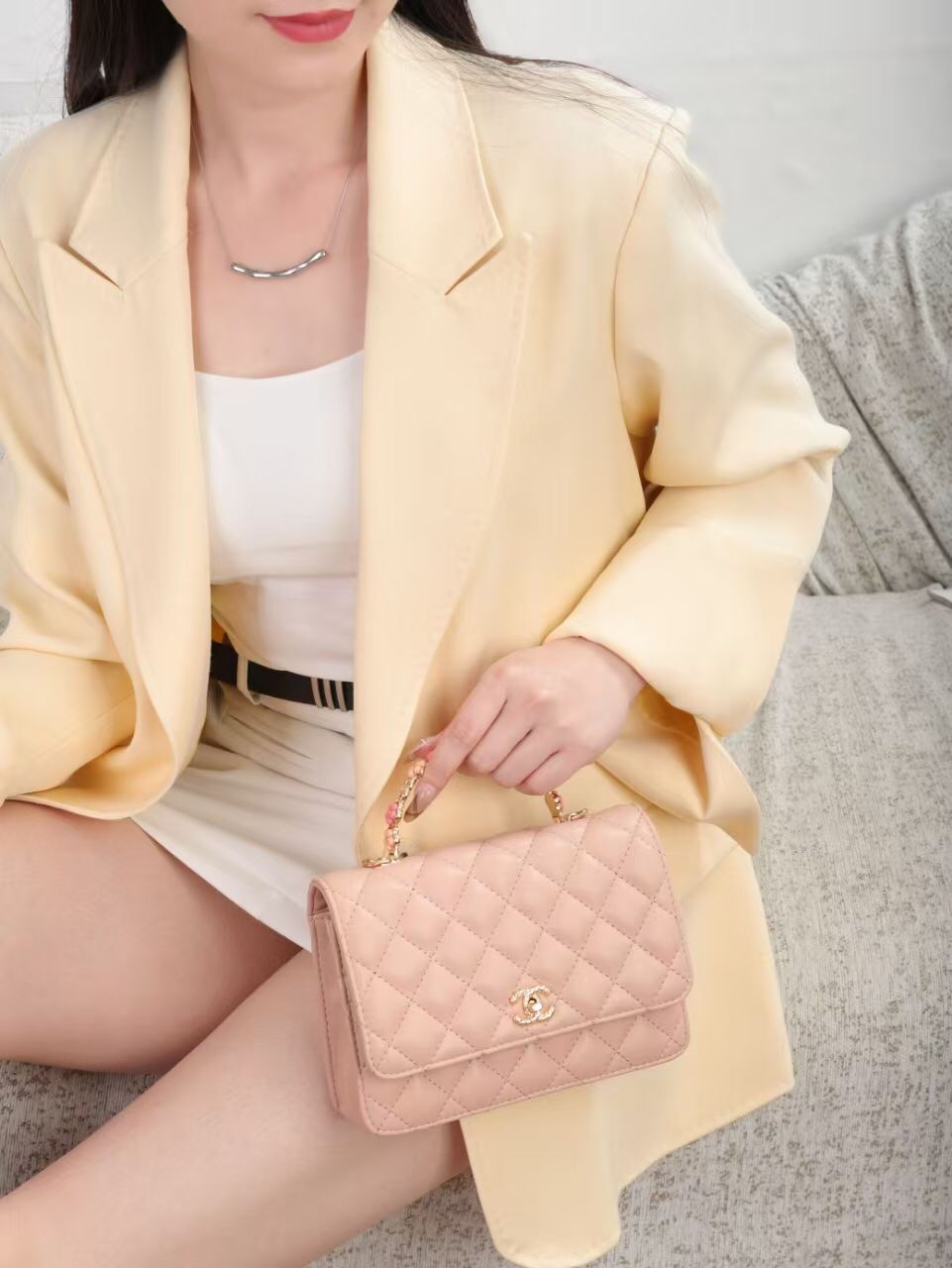 Model wearing blazer holding soft pink Chanel quilted flap bag with top handle