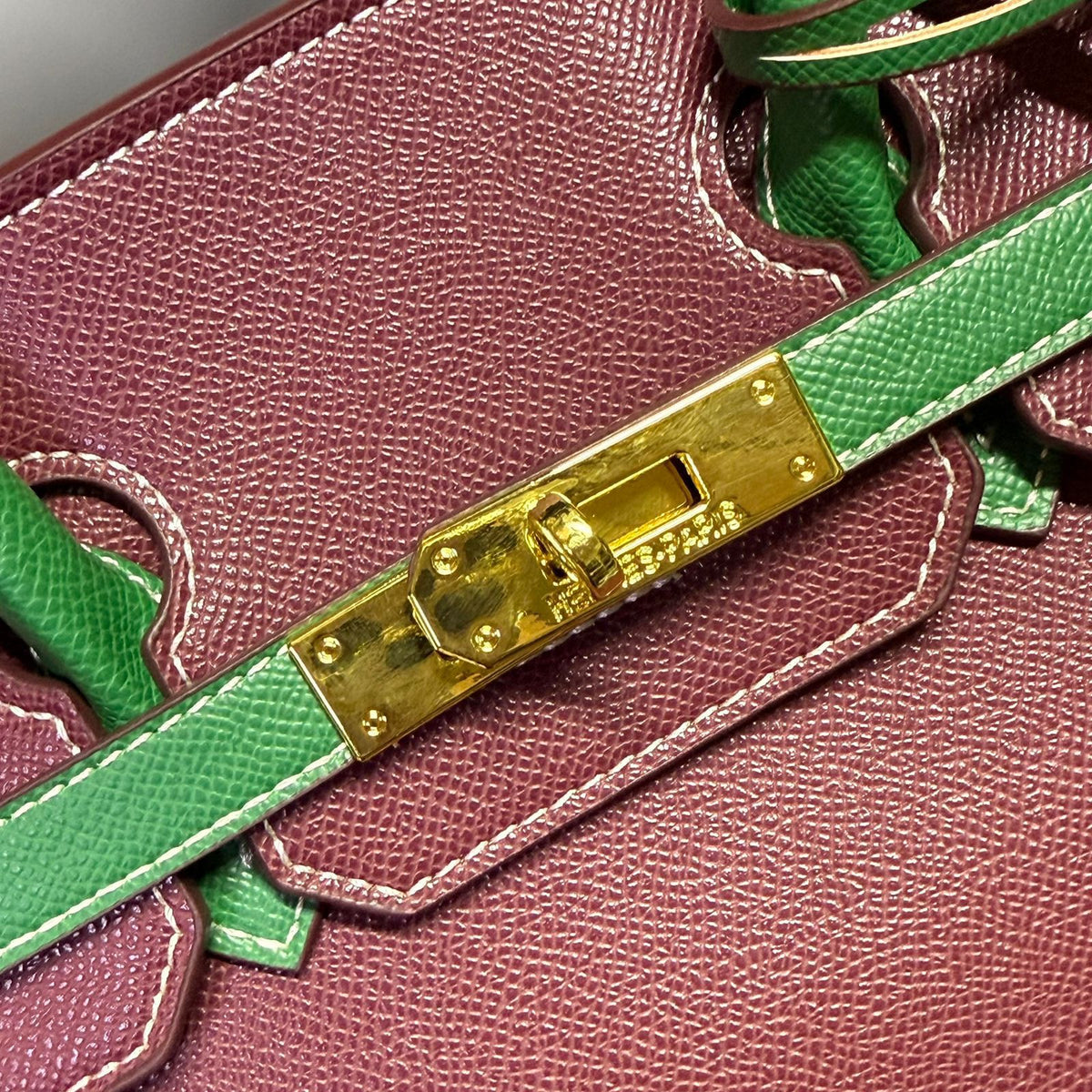 Gold padlock mechanism and green leather belt detail on luxury handbag