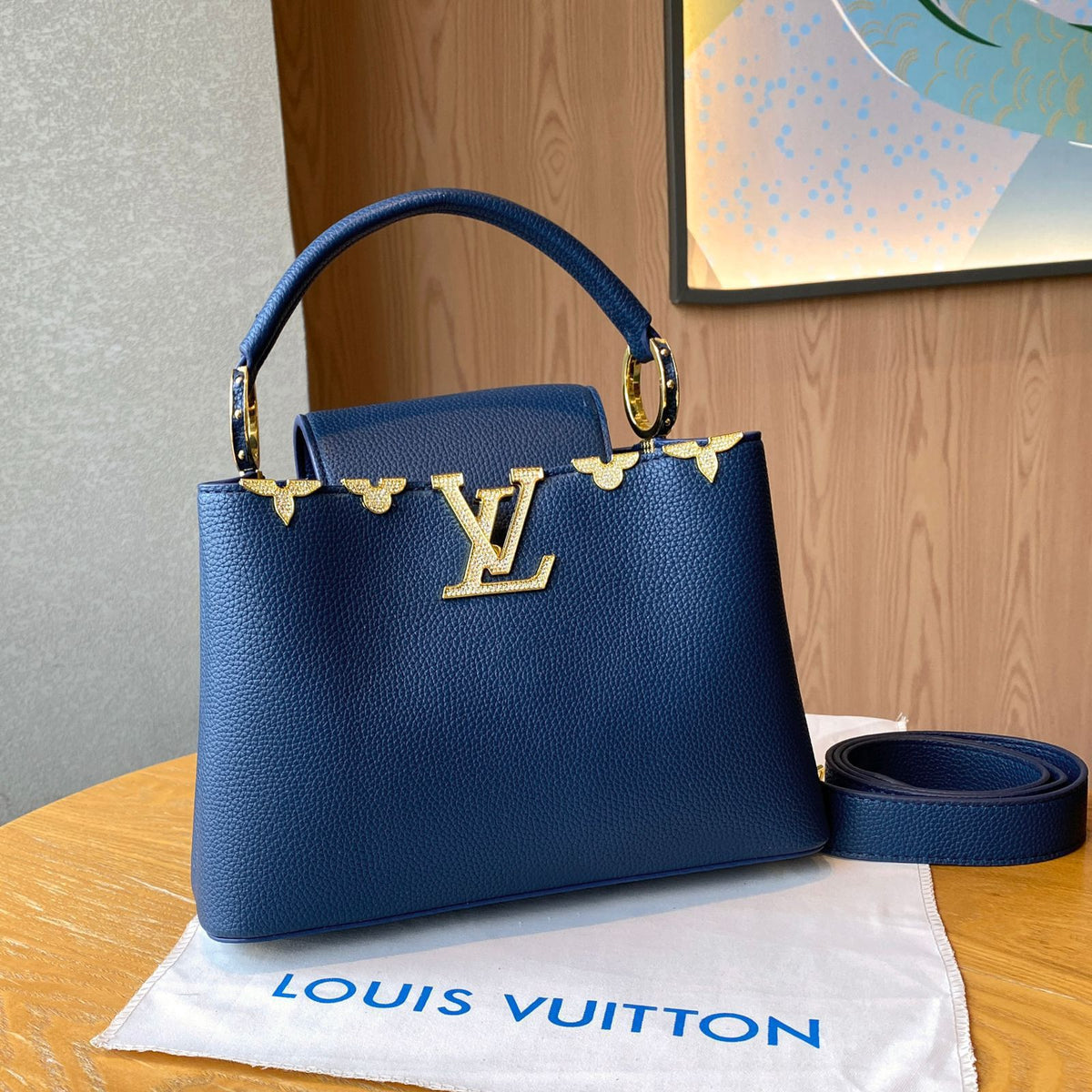Blue handbag with gold accents on a Louis Vuitton dust bag against a wooden background