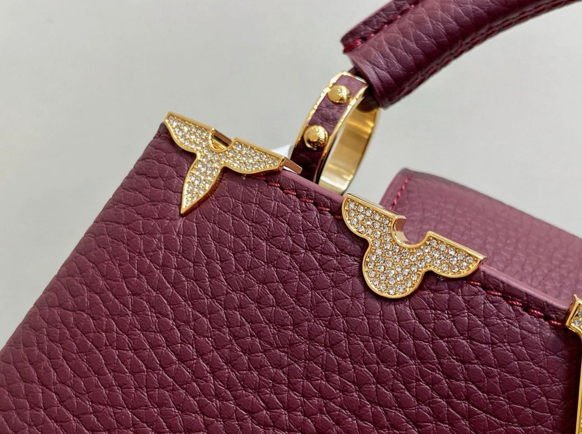 Close-up of a burgundy handbag with gold handles and decorative elements on a light gray background