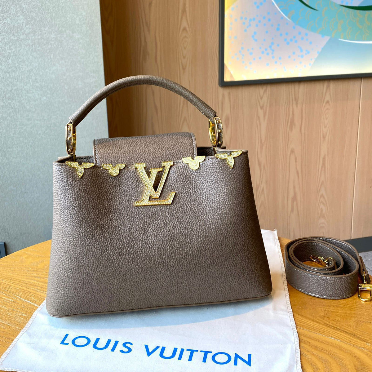 Louis Vuitton handbag with gold hardware on a Louis Vuitton dust bag and wooden surface.