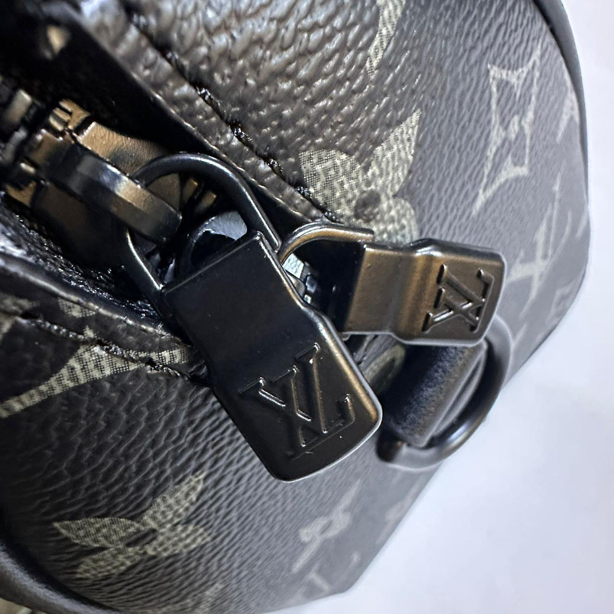 Close up view of metallic zipper pull with engraved Louis Vuitton logo