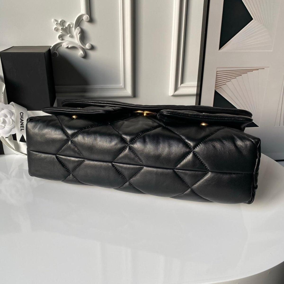 Top and side view of luxury black quilted leather flap shoulder bag resting on display