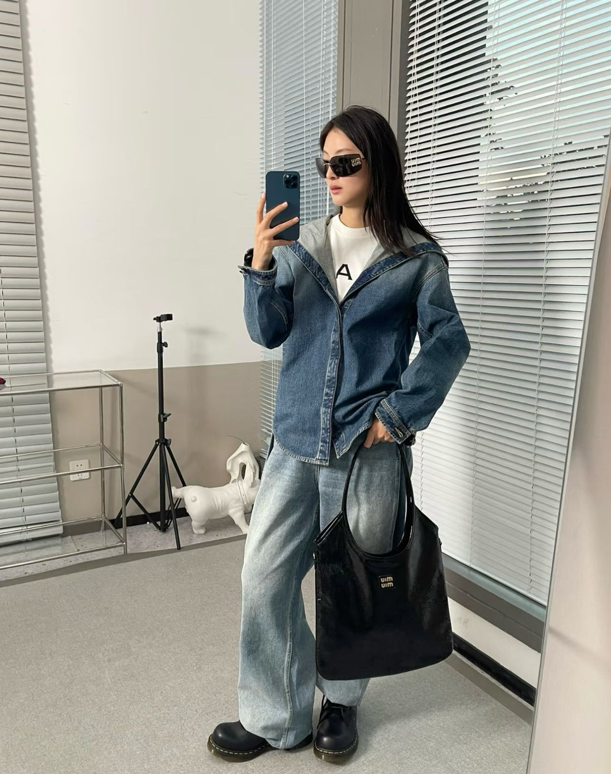 Model carrying black Miu Miu glossy leather tote bag with casual denim outfit
