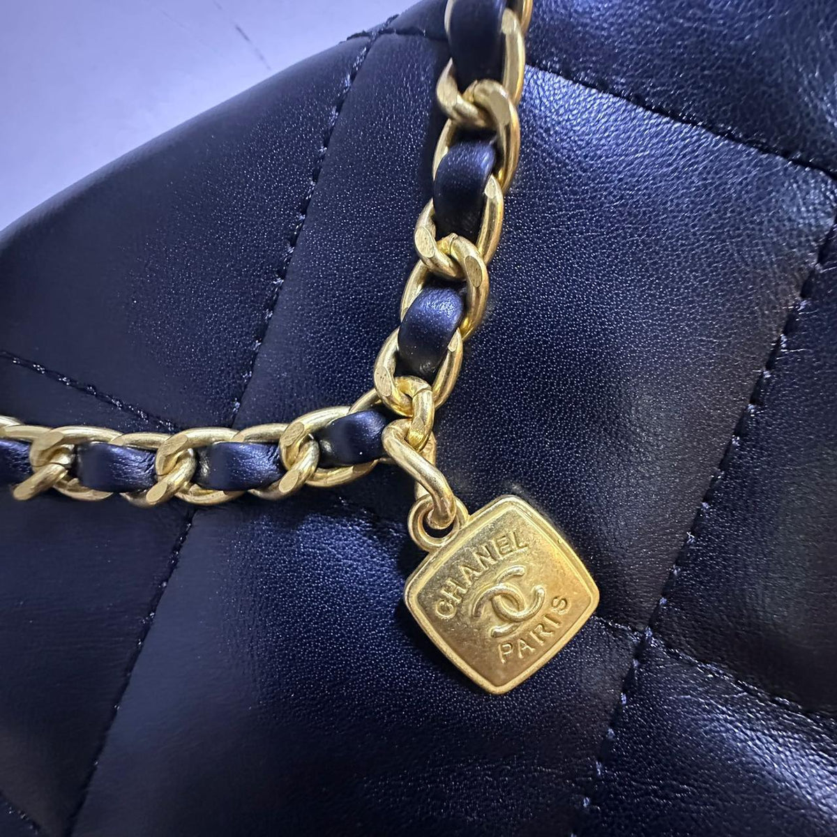 Close up view of woven gold chain strap with metallic logo charm pendant