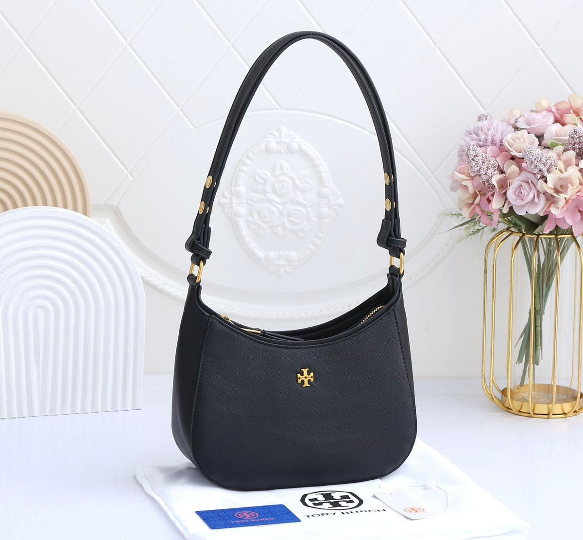 Black handbag with a visible brand logo on a white surface with flowers in the background