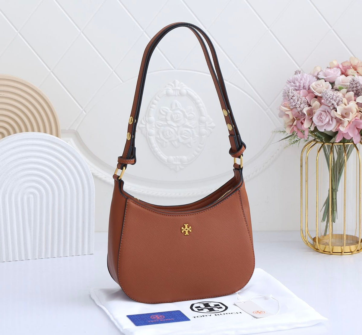 Brown handbag with a visible brand logo on a white surface with a decorative vase in the background.