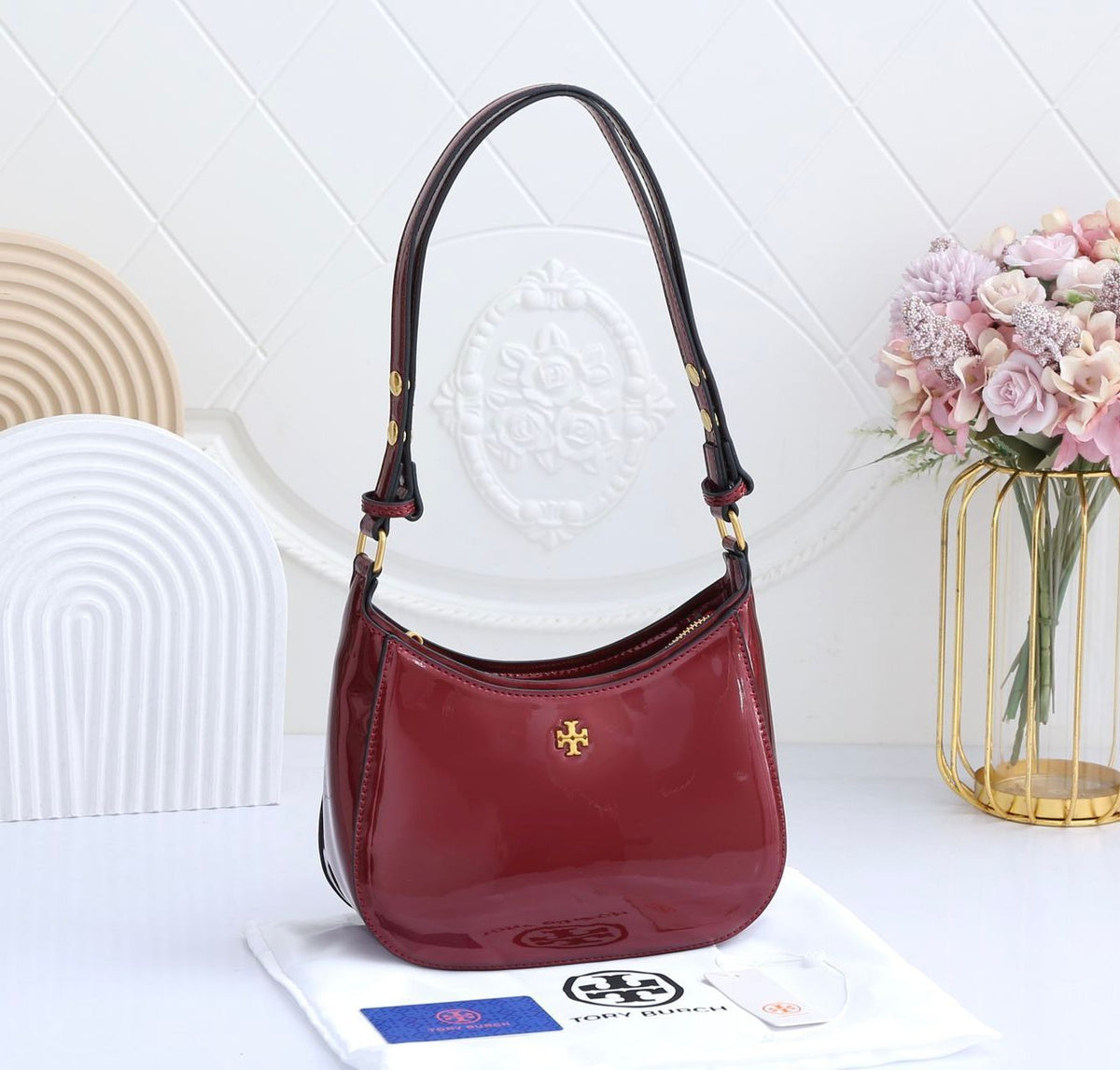 Red handbag with gold accents on a white surface with a decorative background