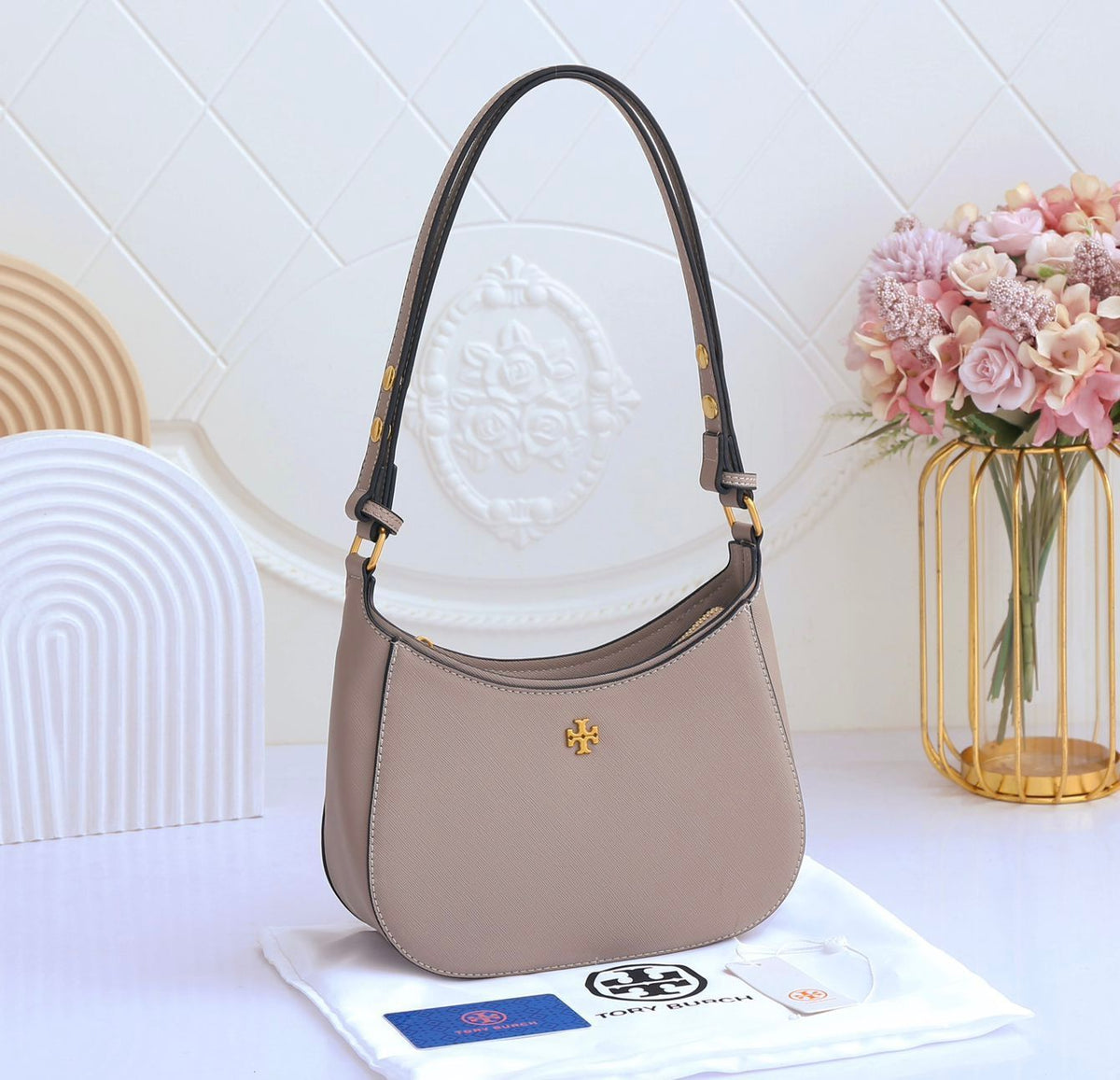 Gray handbag with a brand logo on a white surface with decorative elements.