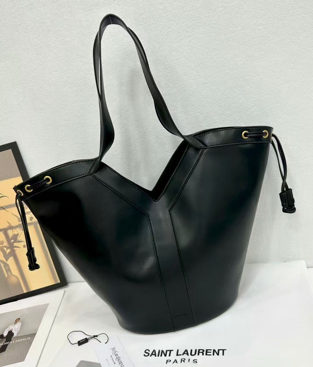 Black leather handbag with drawstring on a white surface, featuring Saint Laurent branding.