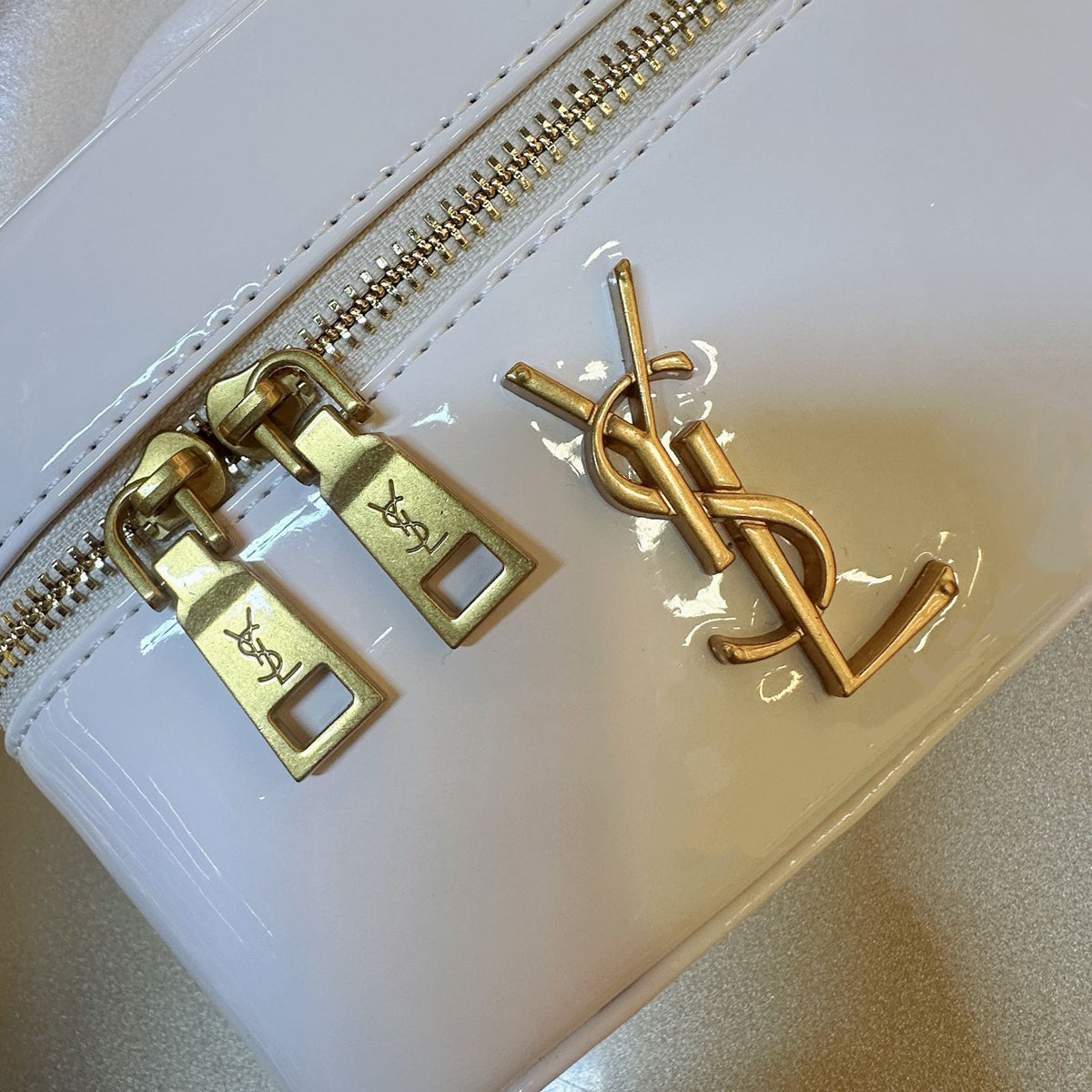 Close up of gold metal YSL monogram charm and double zipper